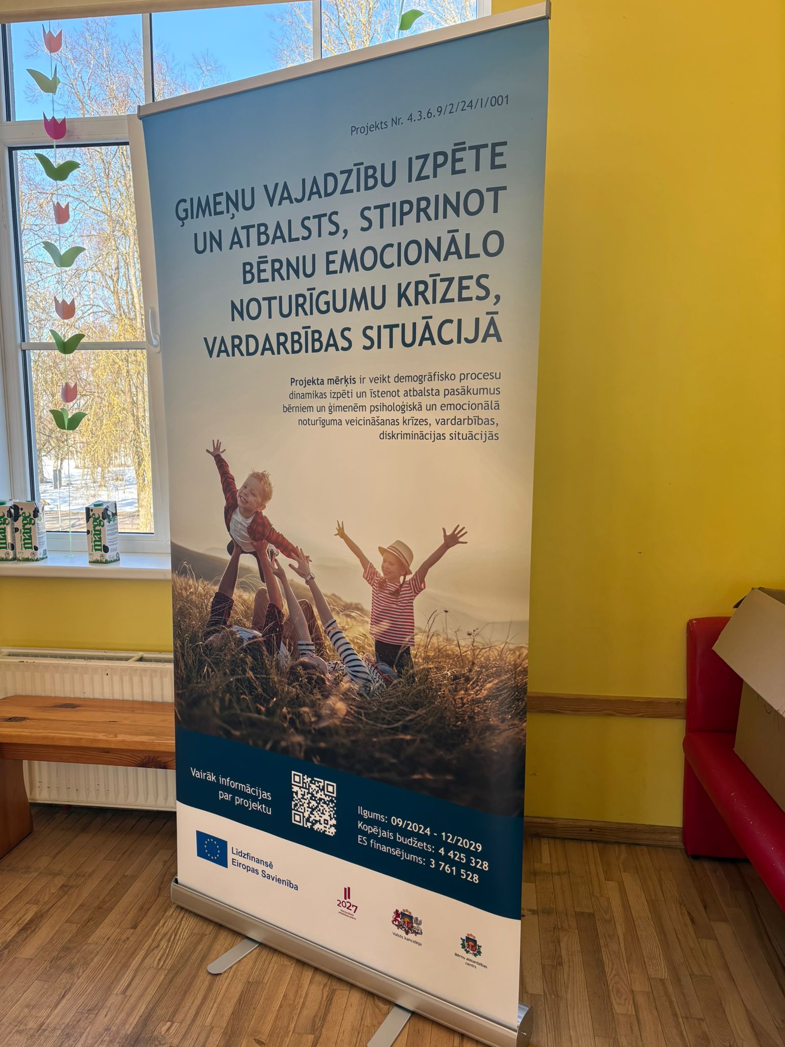 **ALT teksts (mājaslapai):** Roll-up stends Vecsaules pamatskolas telpās ar informāciju par projektu par ģimeņu vajadzību izpēti un atbalstu bērnu emocionālās noturības stiprināšanai krīzes un vardarbības situācijās.  **Nedaudz aprakstošāks ALT teksts (ja vajag pieejamībai):** Vecsaules pamatskolas telpā novietots roll-up stends ar projekta informāciju par ģimeņu vajadzību izpēti un atbalstu bērnu emocionālās noturības stiprināšanai krīzes, vardarbības un diskriminācijas situācijās.  Ja vēlies, varu arī uzrakstīt **SEO optimizētu attēla aprakstu mājaslapai**, kas palīdz labāk parādīties Google rezultātos.